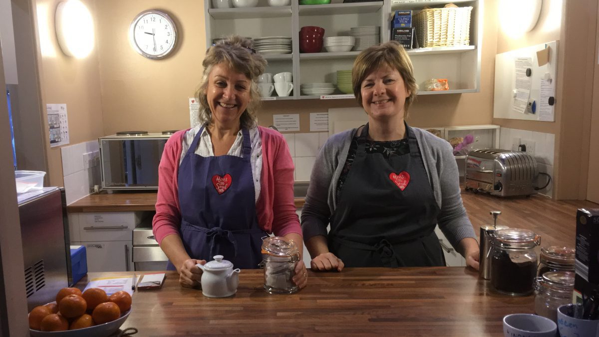 Rhiannon (cafe manager; right) together with a cafe volunteer (left), standing together in the cafe kitchen.