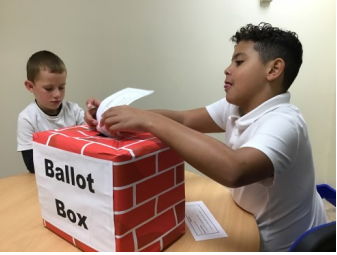Two children from Hoole Primary School putting a slip of paper in a ballot box.