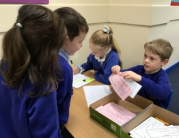 Two children from Hoole Primary School helping another two children with their voting slips.